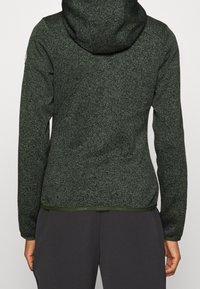 Dunkelgrüne, strukturierte Kapuzenjacke mit figurbetonter Passform, ausgestattet mit kontrastierendem Saum, Bündchen und sichtbaren Nähten, entworfen für Komfort und zum Lagenlook.