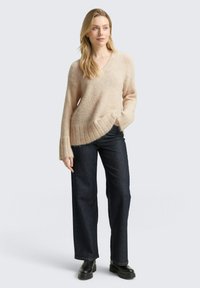 Beżowy sweter na drutach z dekoltem w serek, ściągaczami na mankietach i u dołu, zestawiony z ciemnoniebieskimi, szerokimi spodniami jeansowymi oraz czarnymi botkami na platformie.