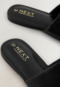 Juodi šlepetės su lygiu paviršiumi ir minkštu padu. Vidinėje dalyje yra užrašas "NEXT FOREVER COMFORT" auksinėmis raidėmis.