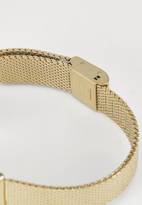 Gold mesh watch band featuring a smooth, metallic clasp with engraved details, showcasing a textured pattern throughout its length.