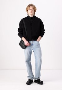 Cardigã de malha preta com botões, combinado com jeans de denim azul claro. Uma bolsa cruzada preta e sapatos pretos robustos completam o visual.