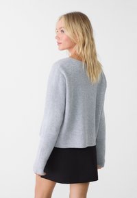 Pullover in maglia a costine grigio chiaro con una vestibilità ampia. Presenta maniche lunghe e un orlo cropped, abbinato a una gonna nera.