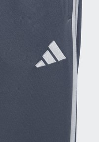Dunkelblaue Sporthose mit einem weißen gestickten Drei-Streifen-Logo auf der linken Seite, glatter Textur und aerodynamischem Design.