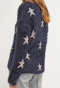 Maglione fuzzy blu navy con motivi a stella argentati, caratterizzato da una vestibilità comoda e maniche lunghe, realizzato in morbido materiale testurizzato.