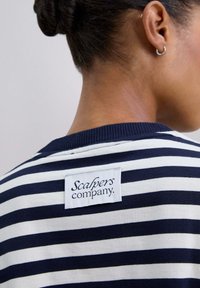 Suéter a rayas blancas y marinas con un cuello de canalé, que presenta una etiqueta de tela rectangular en la parte posterior con la inscripción "Scalpers company".