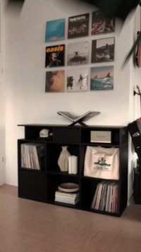 Unità scaffale nera con scomparti a cubo, pieni di dischi in vinile, un vaso decorativo e una borsa di stoffa, posizionata contro una parete bianca.