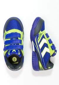 Blauwe en groene kindersport schoenen met een mesh bovenkant, drie klittenbandsluitingen, rubberen zool en witte zigzagaccenten aan de zijkanten.