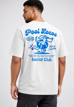 Man wearing white T-shirt with blue print of running dog in float, text "Pool Locos," "Social Club," and event details on back.