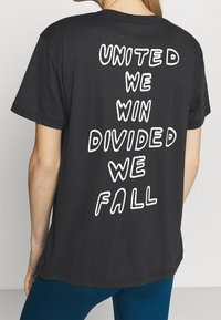 Svart bomulls t-shirt med vit text på baksidan som lyder: "ENADE VINNER VI, DIVIDERAD FALLER VI." Korta ärmar och avslappnad passform.