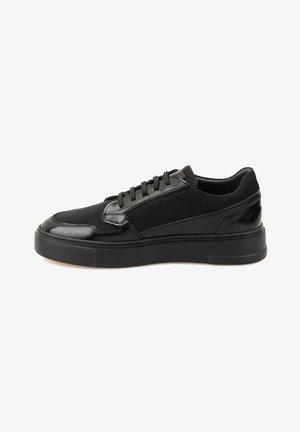 Black sneakers featuring a combination of mesh and glossy synthetic material, round toe, flat sole, and lace-up closure with black eyelets.