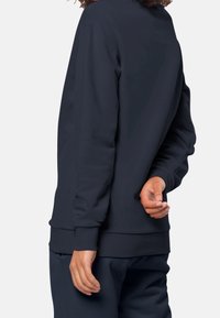 Löysäntuinen tummansininen collegepaita, jossa on ribbireunat hihansuissa ja helmasssa. Pehmeä tekstuuri; pyöreä kaula-aukko ja pudotetut olkalinjat.