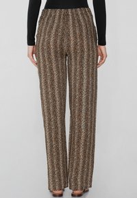 Weite Hosen in braun und beigefarbenem Leo-Muster, mit einem elastischen Bund und einem weichen, strukturierten Stoff. Das Design enthält vertikale Linien.