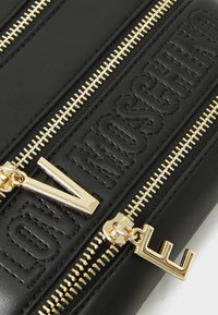 Black leather zip wallet featuring embossed "LOVE MOSCHINO" design, gold hardware, and dual metal zippers with distinctive letter accents.