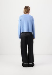 Light blue cropped knit sweater with ribbed cuffs, paired with black wide-leg pants featuring white piping along the seams. Rear view.
