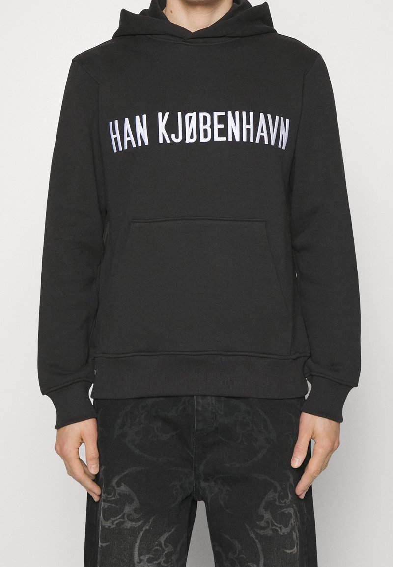 Felpa nera con tasca frontale, con la scritta bianca "HAN KJØBENHAVN". Realizzata in tessuto morbido con polsini e orlo a costine.