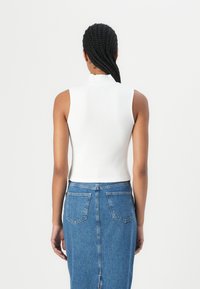 Vit ribbad ärmlös topp med hög krage, tillsammans med en klassisk blå denimkjol med en sprund bak och två bakfickor.