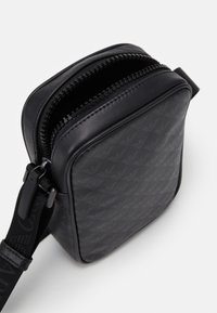 Borsa a tracolla nera con chiusura a zip, caratterizzata da un motivo testurizzato. Realizzata in materiale sintetico, con una tracolla durevole e regolabile.