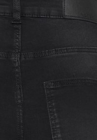 Jeans de ganga pretos com um design ajustado, apresentando uma textura suave, costuras contrastantes e um pequeno bolso traseiro.