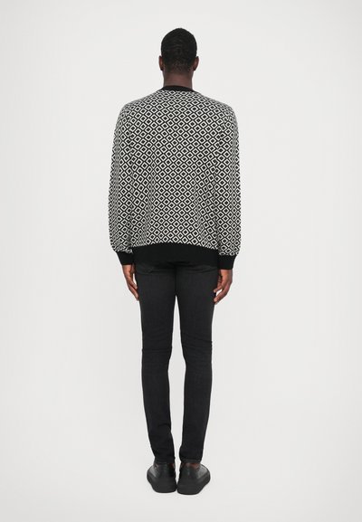 Black and white patterned sweater with a geometric design, paired with black slim-fit jeans and black shoes. Clean, minimalistic aesthetic.