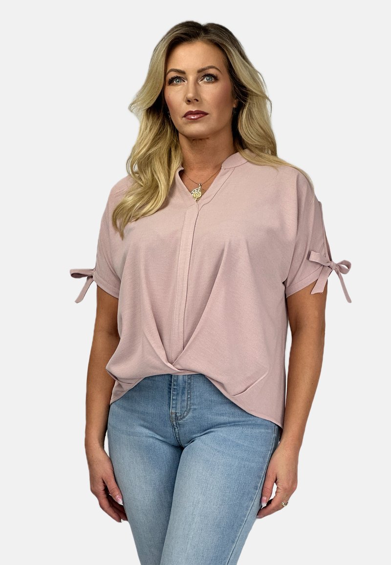 Jasnoróżowa bluzka z kołnierzykiem w kształcie litery V, krótkimi rękawami zdobionymi kokardkami oraz skręconym przodem; zestawiona z jasnoniebieskimi dżinsami.