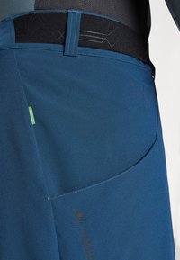 Blue shorts made from recycled material with a textured surface, featuring a black elastic waistband and subtle branding accents.