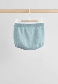 Petits shorts en tricot bleu clair pour bébé avec une taille et des ouvertures de jambes côtelées, suspendus à une barre en bois sur un fond uni.