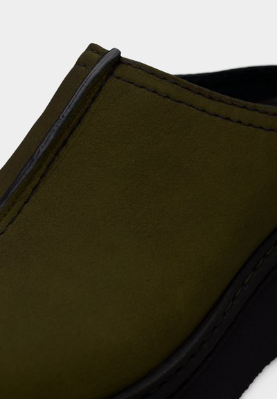 Olívazöld, könnyen felvehető cipő velúr textúrával, fekete varrással és kontrasztos fekete gumitalppal.