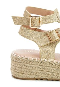 Gold glitter sandals with adjustable ankle straps, featuring a jute-wrapped platform and a smooth leather footbed.