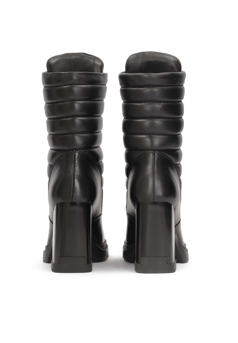 Botas de cuero negras hasta la rodilla con un eje texturizado y acolchado y tacones cuadrados. El acabado suave y el minimalismo en los detalles realzan el diseño.