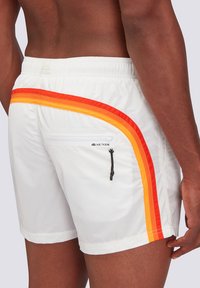 Pantaloni da nuoto bianchi con strisce diagonali arancioni e rosse. Presentano una tasca con zip e una vita regolabile con cordoncino. Tessuto liscio.