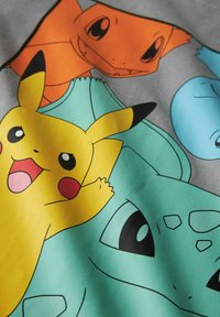 Helle Cartoon-Charaktere Pikachu, Charmander, Bisasam und Schiggy überlappen sich auf einem Stoff mit auffälligen Farben und ausdrucksvollen Gesichtern.