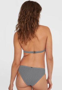 Bikini a righe bianche e nere in tessuto morbido, con fascia regolabile e taglio classico. Presenta una chiusura posteriore e linee pulite.