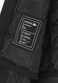 Interno di una giacca nera che mostra un'etichetta nera con testo bianco. L'etichetta include i dettagli del marchio e le istruzioni per la cura, cuciti nel tessuto.