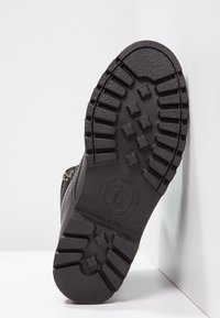 Suela de zapato de goma negra con un patrón de textura para un mejor agarre, bordes redondeados y una impresión de logo circular. Tamaño marcado como 41.