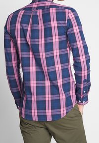 Rutigt skjorta med blå och rosa rutig mönster, knappmanschetter och rundad fåll. Tillverkad av ett mjukt tyg med en bakre veck för bättre passform.