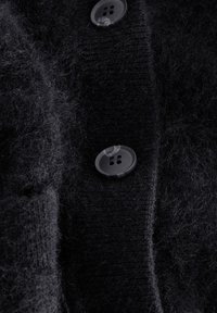 Schwarzer Strickcardigan mit weicher, flauschiger Textur, zwei transparenten Knöpfen vorne und einem gerippten Bündchen.