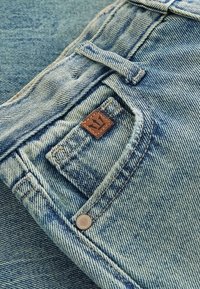 Gros plan d'une poche de jean en denim bleu avec une petite pièce en cuir marron et un détail de rivet en métal.