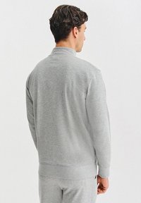 Szara bluza z wysokim kołnierzem, długimi rękawami i ściągaczami na mankietach. Materiał wydaje się miękki o gładkiej fakturze. Widoczne detale szwów.