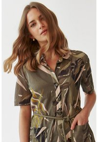 Abito camicia con motivo camouflage in verde e beige, caratterizzato da un colletto, maniche corte, bottoni frontali, vita con cintura e tasche.