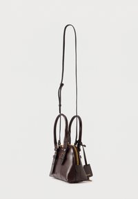 Σκούρα καφέ δερμάτινη τσάντα χειρός με διπλές λαβές, μακρύ ρυθμιζόμενο λουρί, χρυσό φερμουάρ και μία μικρή ετικέτα κρεμαστή, σε απλό ανοιχτό φόντο.