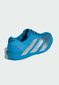 Sininen urheilukenkä, jossa on teksturoitu verkkomateriaali, hopeiset yksityiskohdat ja tyylikäs muotoilu. Varustettu nauhoilla ja pehmeällä kauluksella mukavuutta varten.