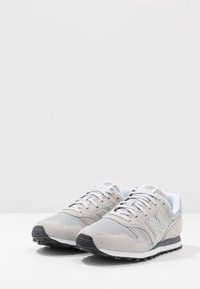 Baskets de sport grises mettant en avant un mélange de matériaux en daim et en maille, avec une surface texturée, un bout arrondi et une semelle en caoutchouc noir contrastante.