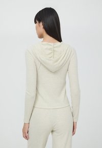 Jasno beżowy, ribbed hoodie o miękkiej fakturze, z długimi rękawami i zwisającym kapturem. Tył ma subtelny detal szwu.