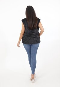 Czarna futrzana bluzka bez rękawów z teksturowanym wzorem, w połączeniu z niebieskimi obcisłymi dżinsami i przezroczystymi wysokimi obcasami. Widok od tyłu.