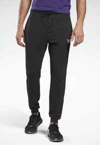 Black sweatpants made of soft material, featuring an elastic waistband with drawstring, tapered legs, and a small Reebok logo.