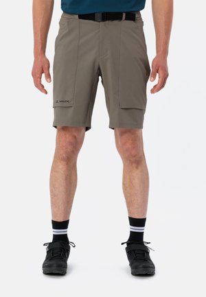 Shorts légers, couleur sable, avec une coupe droite, deux poches latérales et une ceinture noire. Associés à des chaussures noires et des chaussettes rayées.