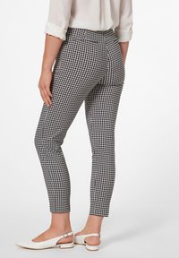 Pantalons à motifs Vichy noir et blanc avec une coupe slim, taille mi-haute et longueur cheville, associés à des chaussures à talons ouverts blanches.