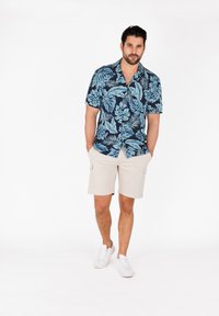Korte mouwen overhemd met een marineblauwe achtergrond en een groot lichtblauw tropisch bladerenpatroon, gecombineerd met beige cargoshorts en witte sneakers.
