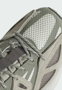 Light gray athletic shoe with mesh, suede, and rubber materials. Features reflective accents, textured overlays, and thick laces.