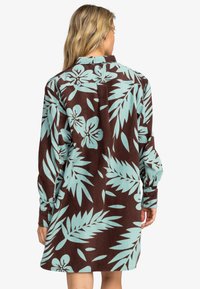 Brown corduroy dress with light blue floral and leaf pattern, long sleeves, button cuffs, and a back pleat for additional movement.